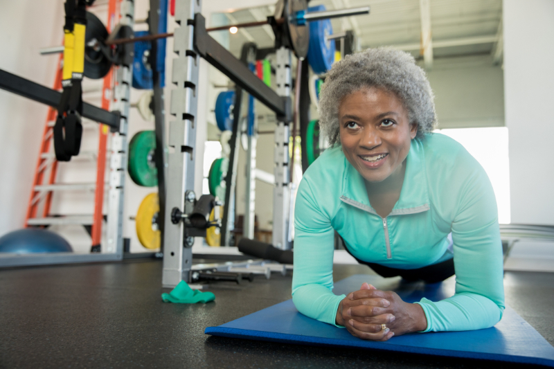 Senior woman smiling while doing a planking exercise in modern gym 